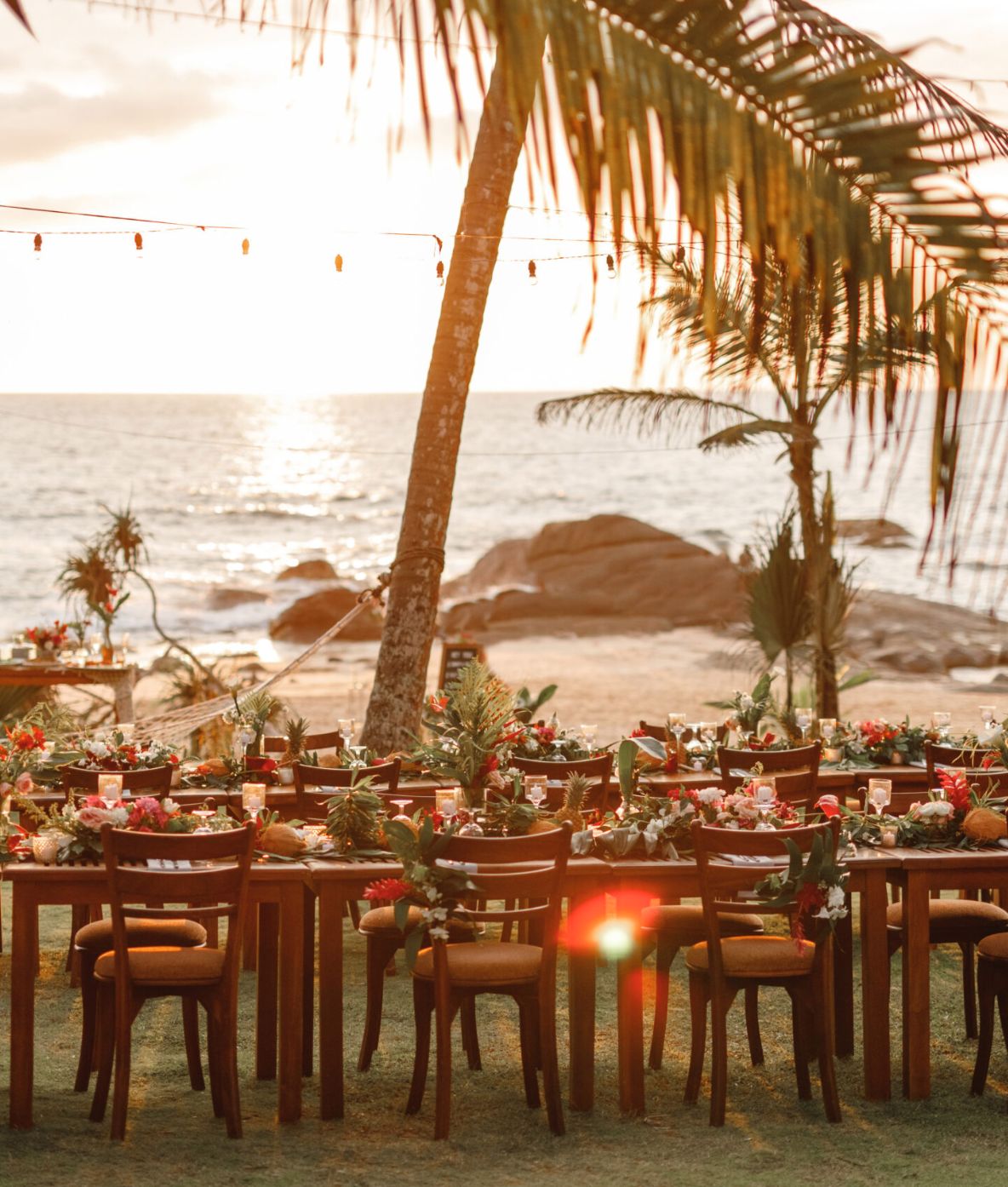 Wedding reception tables set under palm trees at sunset